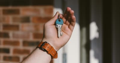 A persons hand holds up a house key against a brick background